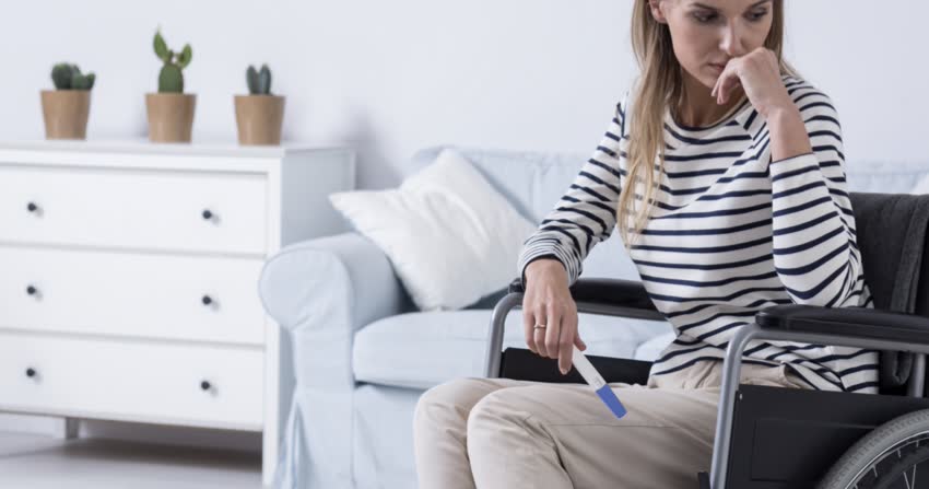 Ragazza in sedia a rotelle con sclerosi multipla con test di gravidanza in mano