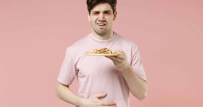 Uomo che regge un piatto di arachidi che mostra evidenti segni di reazione allergica