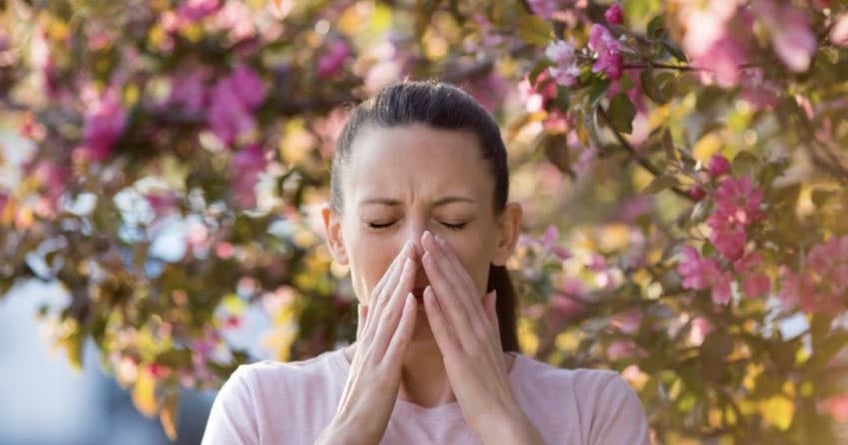 Donna con allergia e sullo sfondo piante in fiore