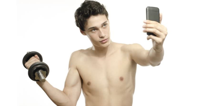 Giovane ragazzo che si scatta un selfie mentre regge un peso per fare i muscoli