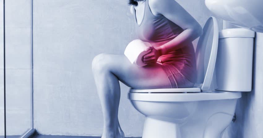 Donna seduta sul wc con sintomi dolorosi da cistite indicati da alone rosso in zona pubica