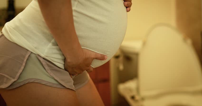 Persona in gravidanza che regge la propria pancia in bagno