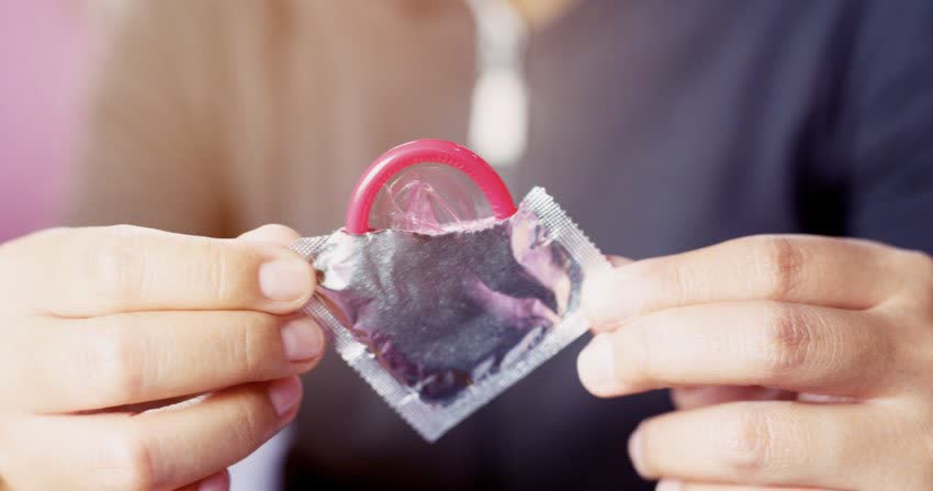 Close up mani che tengono un preservativo rosso che spunta dalla confezione argento