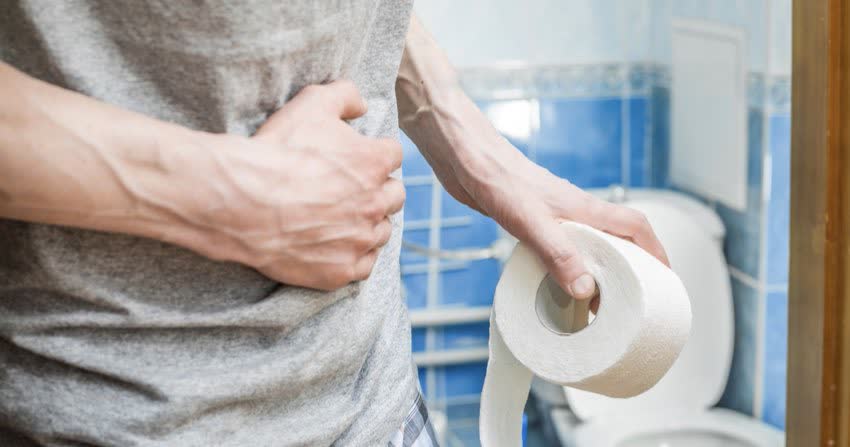 Uomo in bagno con dolori addominali e in mano carta igienica ad indicare problemi intestinali