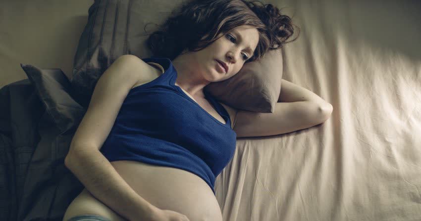 Donna in gravidanza sdraiata a letto in penombra per indicare insonnia