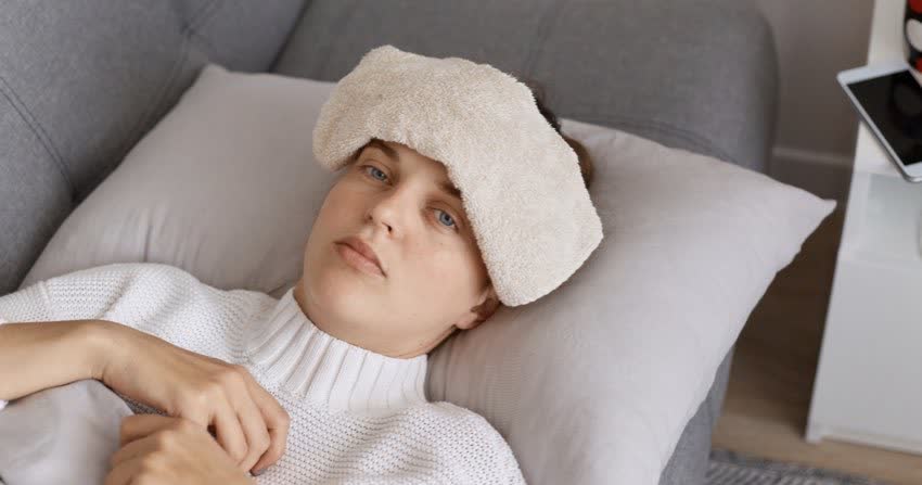 Donna con sinusite stesa sul divano con pezza calda sulla fronte