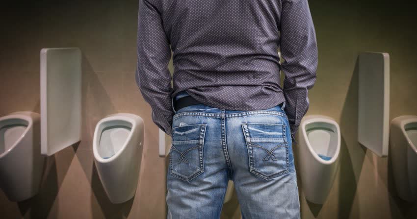 Uomo in piedi di fronte ad urinatoi