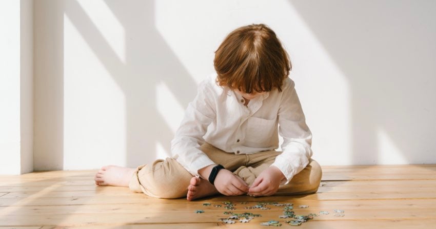 Bambino seduto sul pavimento che costruisce un puzzle