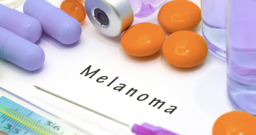 Scritta melanoma su sfondo bianco circondata da farmaci e siringa