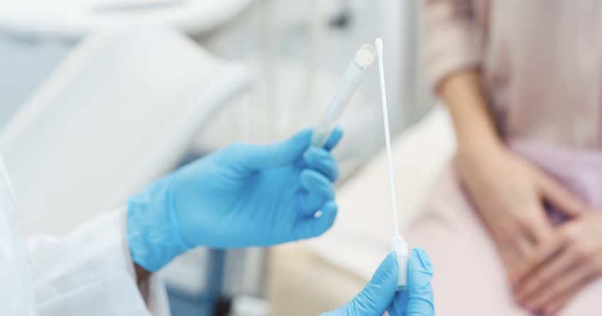 Medico che inserisce campione vaginale all'interno del tubo di analisi con sullo sfondo una paziente