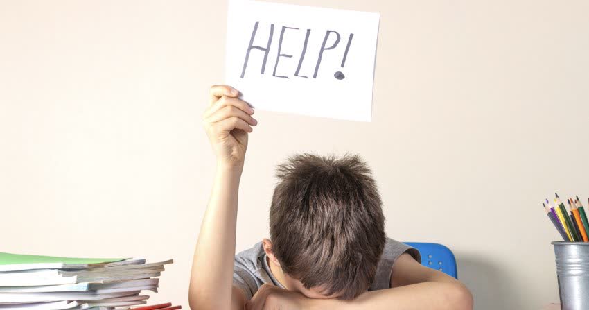 Bambino sotto stress tra i compiti che regge un cartello con la scritta aiuto