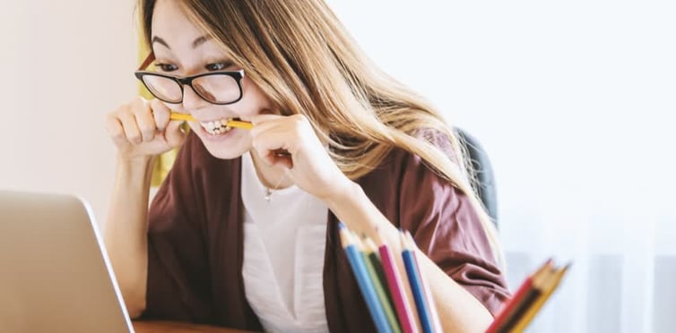 foto di ragazza con gli occhiali davanti al computer mentre morde una matita o penna gialla perché stressata - colpita da stress