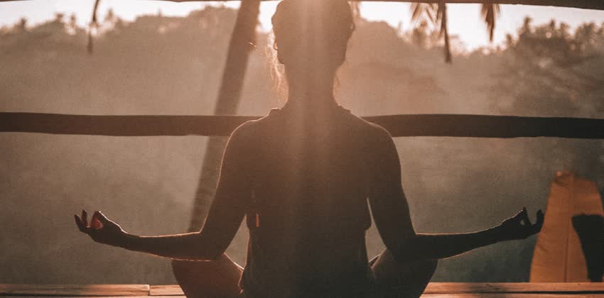 foto di donna di spalle mentre fa meditazione e yoga al sole per combattere lo stress